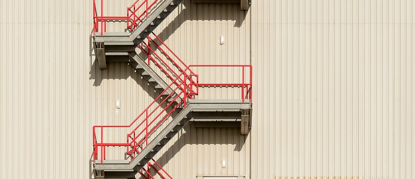 Rote Brandschutztreppe an einer beigen Gebäudewand 