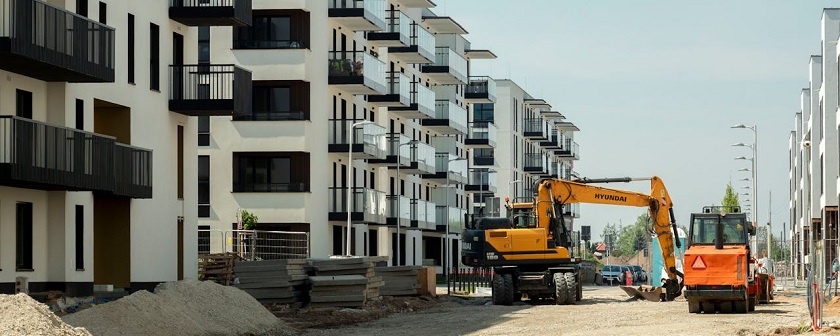 Neubauhäuser mit Balkonen und einer unfertigen Straße mit einem Kran und Bagger darauf